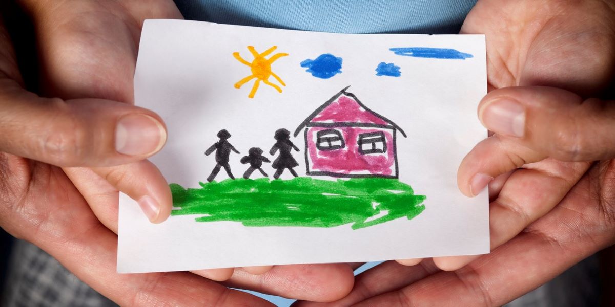 Close up of child and parent hands holding drawing of house and family