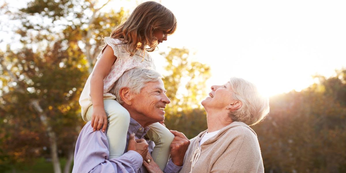 Grandparents and grandchild smiling outdoors. Grandfather carrying child on his shoulders